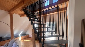 Et loftrum med træbjælker, en trappe, en hvid sofa og et spisebord.