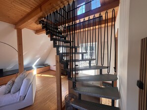 Ein Loft-Zimmer mit Holzbalkendecke, einer Treppe, einem weißen Sofa und einem Essbereich.