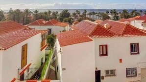 A coastal residential area with white buildings and red-tiled roofs, a clear sky, and a view of the sea. - Apartment in Playa de las Americas - Swimming pool, garden and excellent location (Arona)