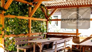 En pergola av trä med bänkar och bord, klätterväxter som växer på konstruktionen och en skylt med texten ”Eifel-Quartiere”.