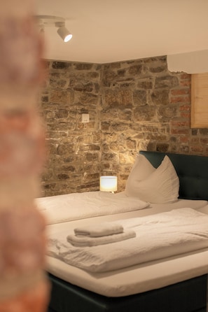 A bedroom with a stone wall, a bed with white linens, and a bedside lamp. - Our small but charming holiday home offers everything you need (Antweiler)