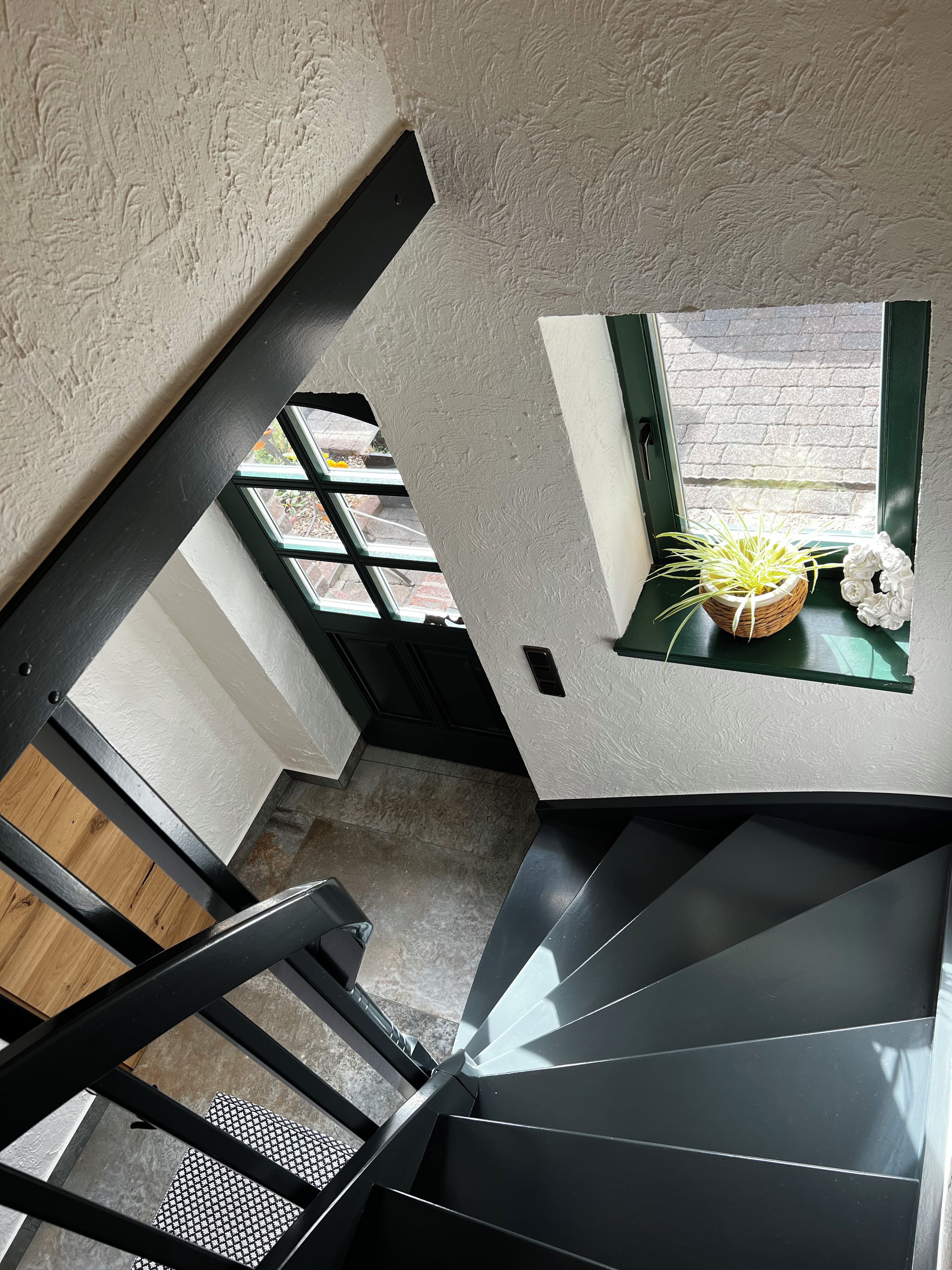 Ein modernes Interieur mit einer Treppe, einem Fenster mit Blick auf die Straße und einem kleinen Tisch mit Pflanze und Dekoration.