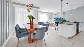 Eine moderne Küche mit einer zentralen Kochinsel, einem Essbereich mit Holztisch und Stühlen sowie ein Wohnbereich mit Fernseher und Sitzgelegenheiten.