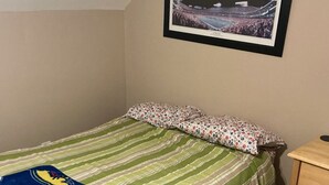 Ein Einzelbett mit gestreifter Bettdecke und einem Kopfkissen mit Blumenmuster. Über dem Bett hängt ein gerahmtes Bild an der Wand.