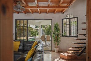 A living room with a leather sofa, a potted plant, a staircase, and a view through a glass door. - Luxury Private Compound w/ Pools, 20 person Jacuzzi and 5 min walk to the beach (Cabarete)
