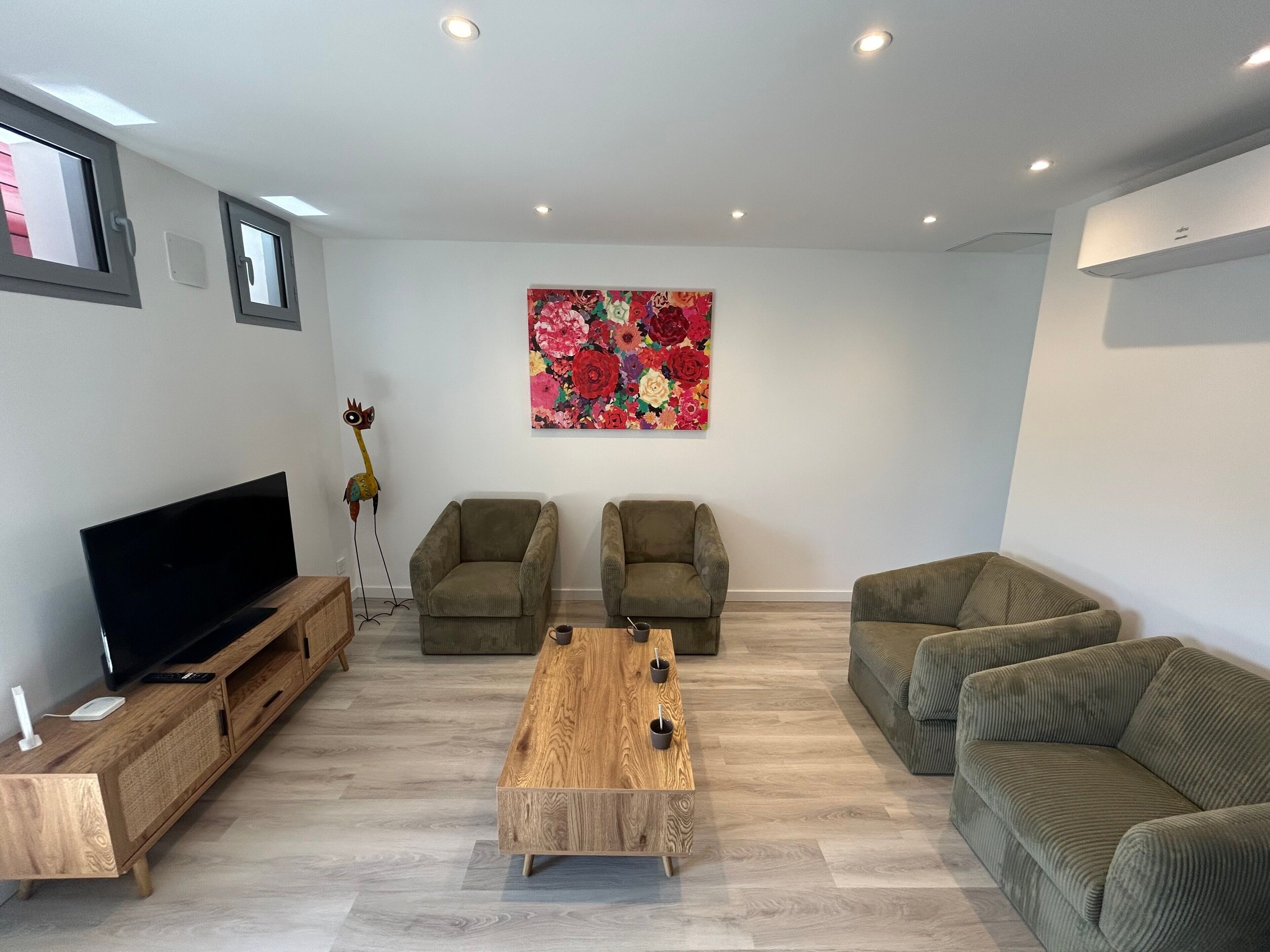 Un salon équipé d’un téléviseur à écran plat, de deux fauteuils, d’un canapé, d’une table basse et d’un tableau représentant des motifs floraux accroché au mur.