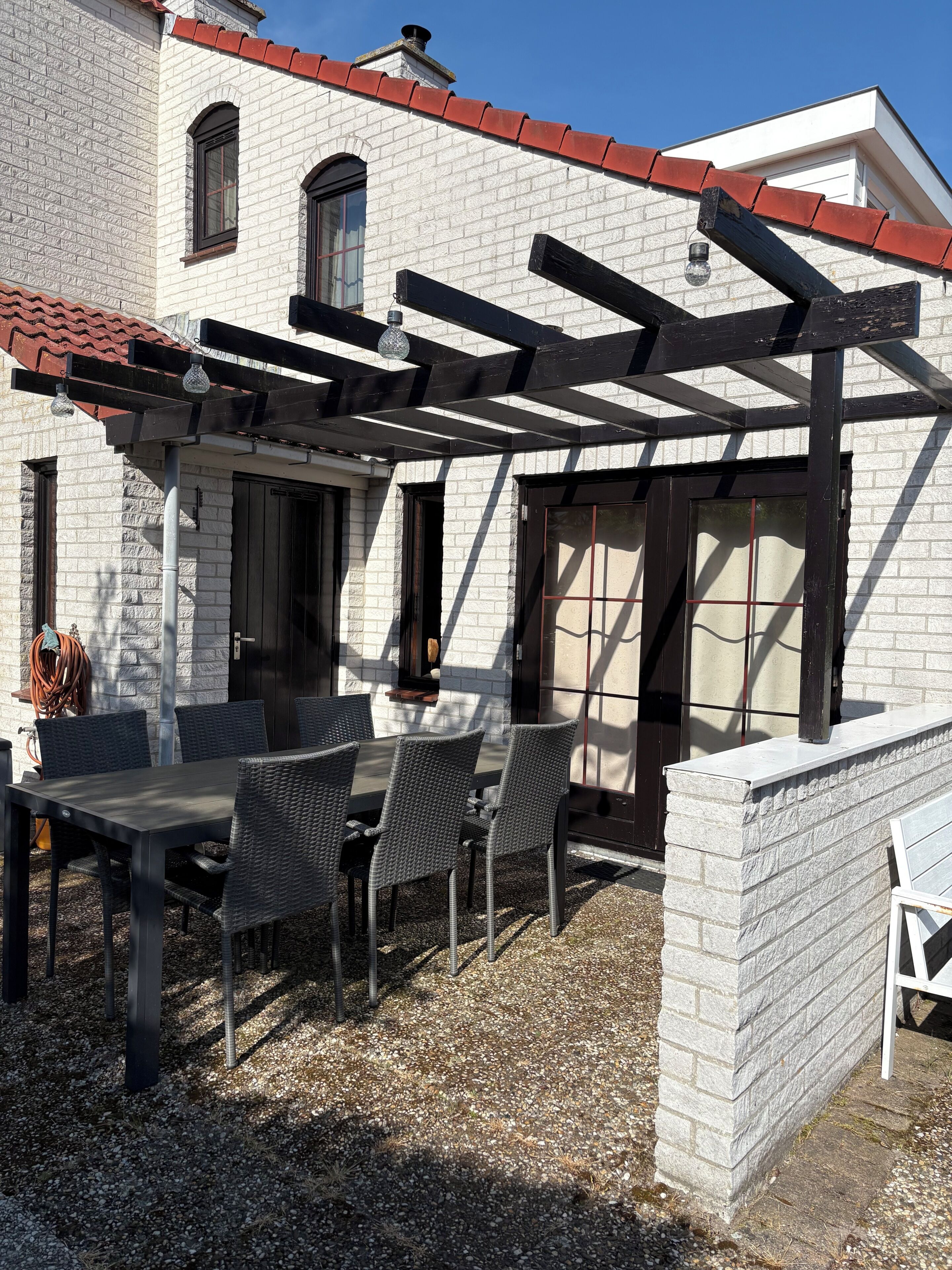 Une terrasse avec une pergola, une table et des chaises, un mur en briques et une fenêtre.