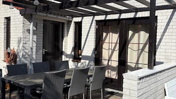 Une terrasse avec une pergola, une table et des chaises, un mur en briques et une fenêtre.