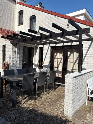 Un patio con una pérgola, una mesa, sillas, un muro de ladrillo y una ventana.