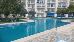 Una piscina con baldosas de piedra, rodeada por un edificio con balcones y un área con césped.