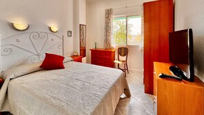 Un dormitorio con cama, televisor, escritorio, silla, cómoda, espejo y ventana.