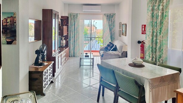 Amplia sala de estar con mesa de comedor, sillas azules, sofá, ventilador de techo y balcón con vista a edificios.