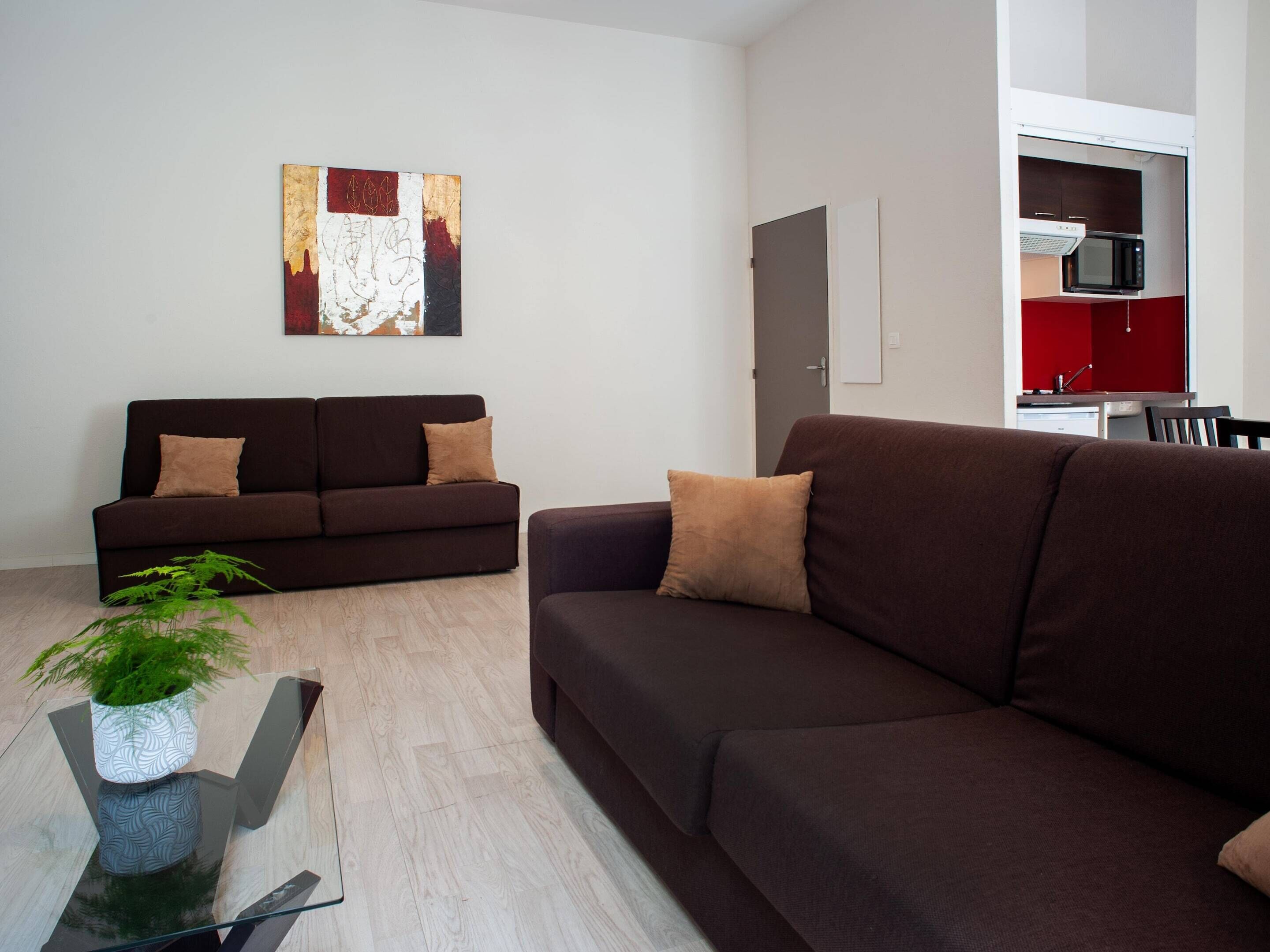 A modern living room with two sofas, a glass coffee table, and a potted plant.