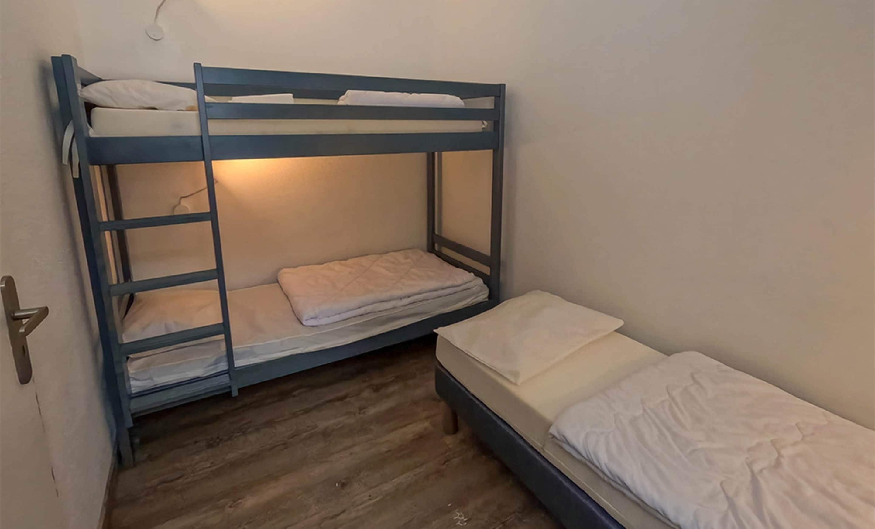 A bunk bed room with a wooden floor, a door, and a wall-mounted light fixture.