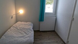 A small, single-bed room with a radiator, a window with curtains, and a wall-mounted light. - 2-bedroom Home in Monts Jura (Lelex)