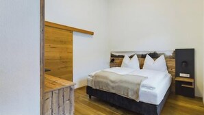 A bedroom with a wooden headboard, a bed with white bedding, a bedside table, and a nightstand.