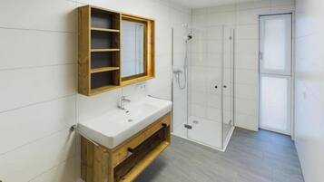 Ein Badezimmer mit einem Holzbadschränken, einem weißen Waschbecken, einem Spiegel und einer Duschkabine aus Glas.