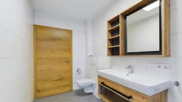 A bathroom with a wooden door, white tiles, a white sink, and a mirror with shelves.