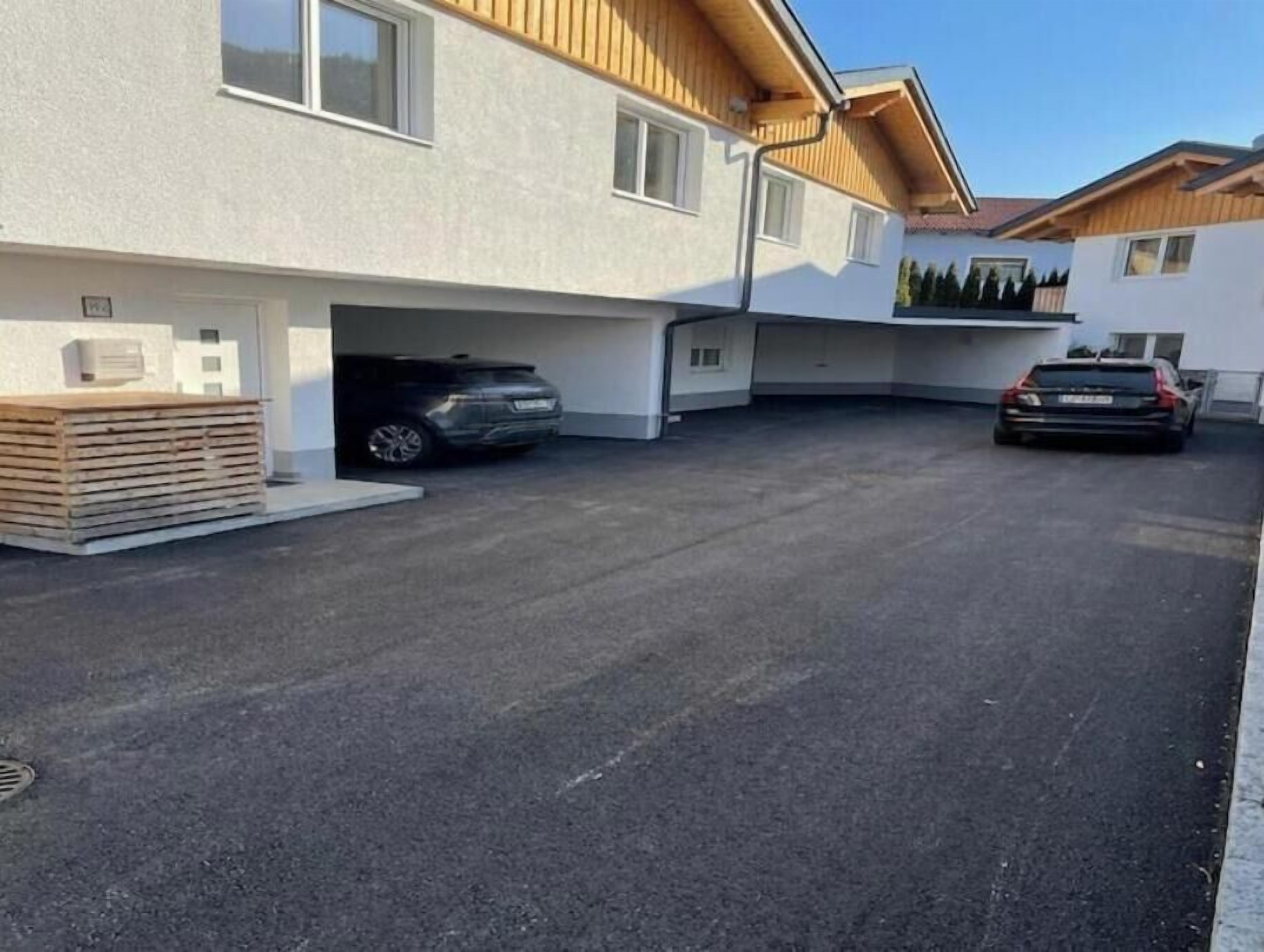 A modern building with a garage, two cars parked inside, and a stack of wooden planks outside.