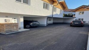 A modern building with a garage, two cars parked inside, and a stack of wooden planks outside.