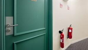 Une porte de couleur bleu-vert avec une plaque de numéro, un extincteur et un luminaire fixé au mur.