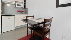 Une petite cuisine équipée d’un four à micro-ondes, d’un petit réfrigérateur et d’un évier. On y trouve une table à manger avec deux chaises et un tapis rouge.