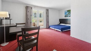 Ein Hotelzimmer mit einem Bett, einem Schreibtisch mit Lampe, einem Sessel und einem Fenster mit Vorhängen.