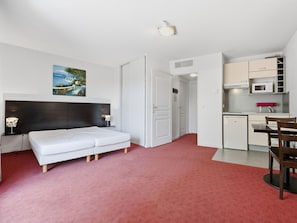 Une pièce de taille modeste comprenant un lit, un bureau et une kitchenette.