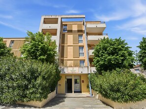 Un immeuble résidentiel à plusieurs étages, doté d’une entrée centrale, de balcons et d’un espace vert environnant.