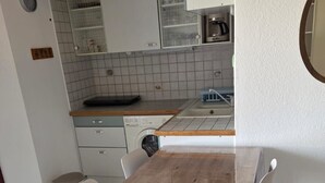 A kitchen with a wooden table and chairs, a washing machine, and a coffee maker. - Bright apartment for 6 people, near the sea (Agde)