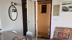 A room with a dining table, chairs, a sofa, a mirror, and a door leading to another room. - Bright apartment for 6 people, near the sea (Agde)