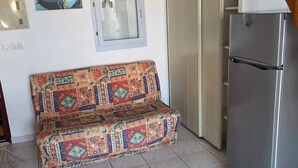 A kitchenette with a refrigerator, a patterned sofa, a window with a view, and a door leading to a balcony. - Bright apartment for 6 people, near the sea (Agde)
