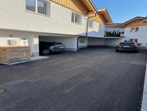 A modern building with a garage, two cars parked inside, and a stack of wooden planks outside. - Bergfeuer Suite Lechtal - modern, stylish & with fantastic mountain views (Stockach)