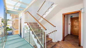 Una escalera con barandillas de vidrio, pasamanos de madera y suelo de baldosas que conduce a una puerta con la inscripción 'ETV'.