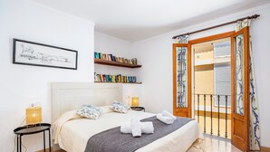 Un dormitorio ordenado con cama, lámparas de noche, una estantería y un balcón con cortinas.
