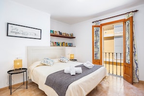 A neatly arranged bedroom with a bed, bedside lamps, a bookshelf, and a balcony with curtains. - 'Voramar 85' Apartment with Sea Views, Wi-Fi, and Air Conditioning (Port de Pollença)