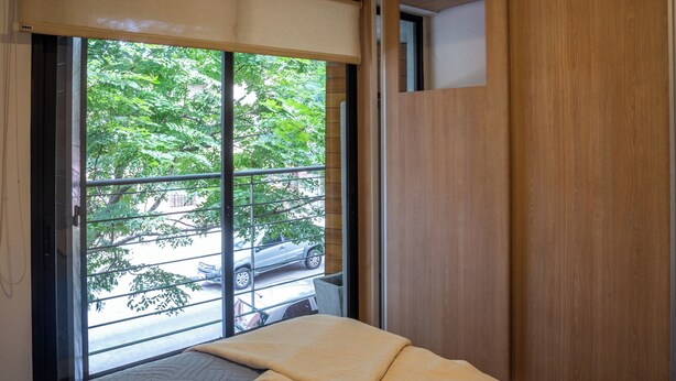 A room with a bed, a window with a view of trees and parked cars, and a wooden door. - House in Pocitos, near the stadium and the promenade (Montevideo)