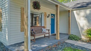 A house with a porch, a bench, a blue door, and a hanging flower basket.