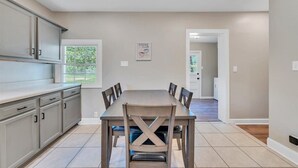 A modern kitchen with a dining table and chairs, light-colored cabinets, and a window.