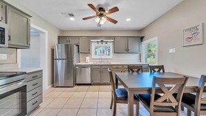 A modern kitchen with a built-in oven, a stainless steel refrigerator, a ceiling fan, and a dining area with wooden chairs and a table.
