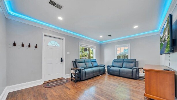 A living room with hardwood flooring, two dark leather sofas, a wooden cabinet, and a door with a window.