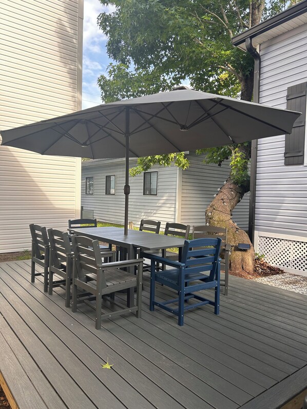 Eine Terrasse im Freien mit Tisch, Stühlen, einem großen Sonnenschirm und einem Baum.