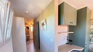 Een hal met een keuken op de achtergrond, een inbouwkeukenkast met een plank, en een deur naar een andere kamer.