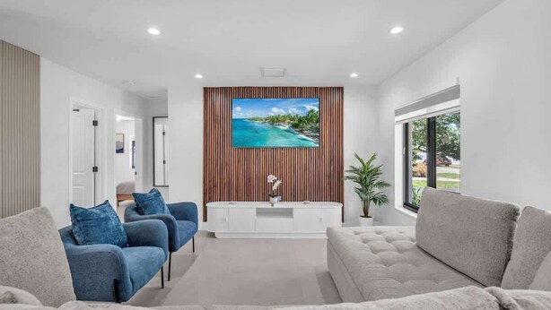 A modern living room with a large flat-screen TV, a white entertainment unit, and two sofas. - Casa Mimosa Family Tropical Oasis with Pool (Miami)