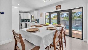 A dining area with a table set for six, a kitchen in the background, and a sliding glass door leading to a pool. - Casa Mimosa Family Tropical Oasis with Pool (Miami)