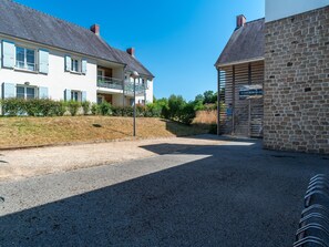 A residential area with a gravel driveway, a two-story house with blue shutters, and a stone building with a sign. - Art Village Apartment for Four (Pont-Aven)