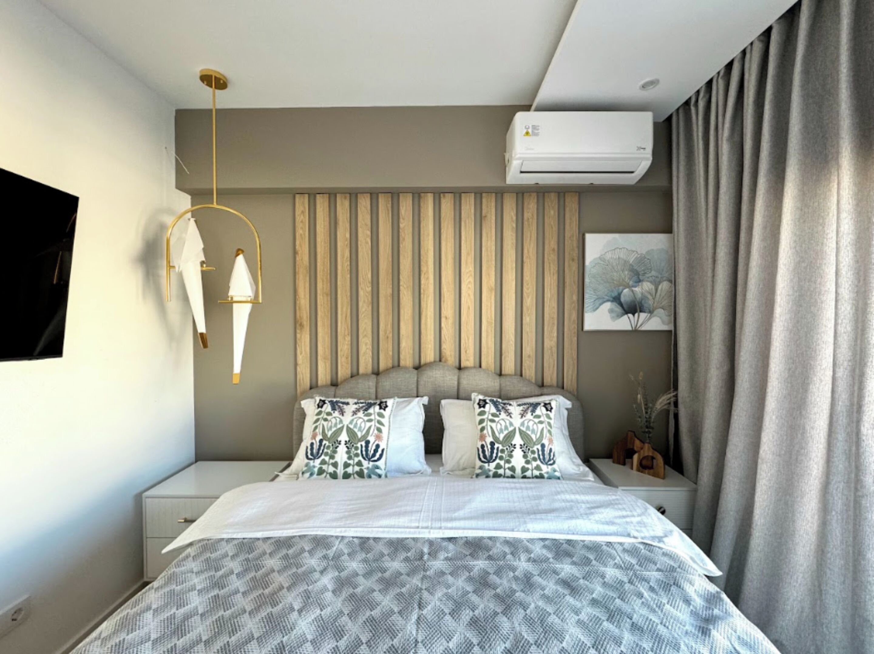 A modern bedroom with a bed, bedside tables, a wall-mounted air conditioner, and a curtain.