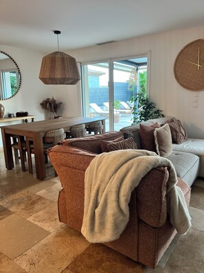 Ein Wohnzimmer mit einem braunen Sofa, einer weißen Decke, einem Esstisch und einem großen Fenster.