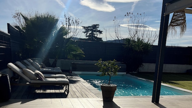 Zona de piscina amb gandules, una planta en test i un pont de fusta.
