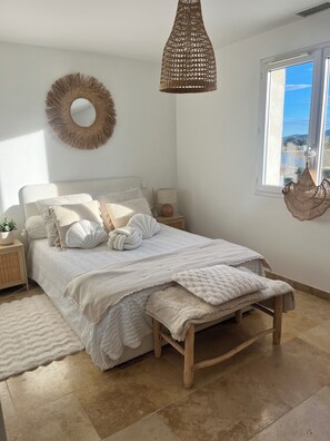 Ein Schlafzimmer mit Bett, Nachttischen, einer Pendelleuchte, einem Fenster und Blick ins Freie.